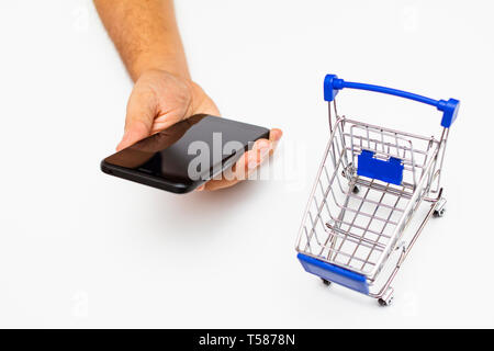 cropped man hands holding a smart phone beside a Mini shopping trolley - online shopping concept Stock Photo