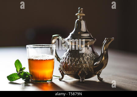 close up of moroccan traditional tea pot and glass cup full of tea - Moroccan tea Stock Photo
