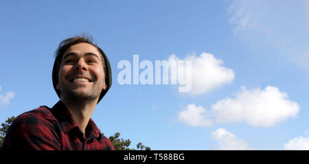 Portrait of an authentic and genuine hipster man smiling on a blue sky with white clouds background. Stock Photo