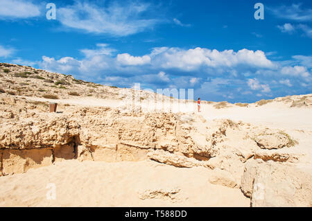 Image of one young white girl standing on a rough limestone cliff near Cape Greco, Cyprus. Many white clouds in the sky, barren orange sandy hill, vas Stock Photo