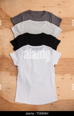 Stack of different coloured womens T-shirt on wooden background. Vertical wiev. Stock Photo