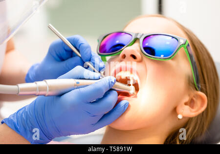 Dental hygienist performing teeth polishing procedure to preteen girl in pediatric dental clinic. Doctor using prophy brush on handpiece to remove har Stock Photo