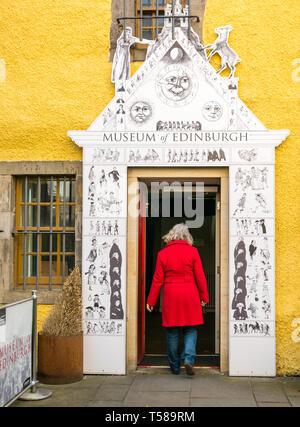 Senior woman wearing red coat entering Museum of Edinburgh, Royal Mile, Edinburgh, Scotland, UK Stock Photo