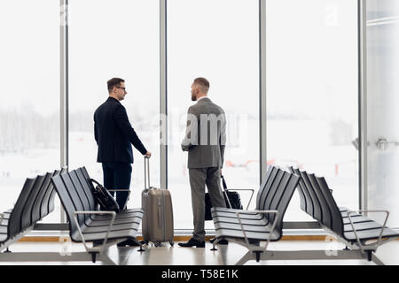 Silhouette of two businessman standing in front of a big window at airport at wating area near departure gate Stock Photo