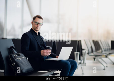 A business man sitting at the airport park working with his laptop and drinking takeaway coffee while waiting the flight departure. Stock Photo