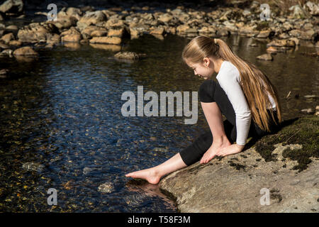 Olallie State Park, near North Bend, Washington, USA. Nine year old girl gingerly testing the coldness of the north fork of the Snoqualmie River, with Stock Photo