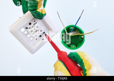 Worker in protective gloves is mounting buttons of two-button light switch with hand tool. Stock Photo