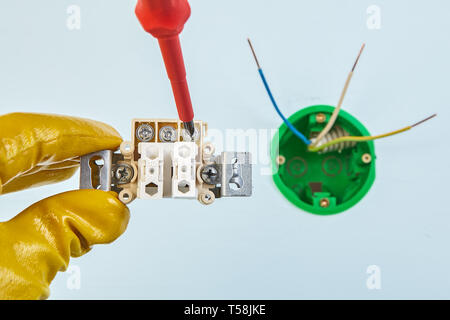 Worker in yellow protective gloves is tightening screw in bouble light switch with round electrical box on the background. Stock Photo