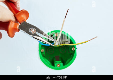 Electrician is installing new round outlet box for wall light with help of long nose pliers. Stock Photo
