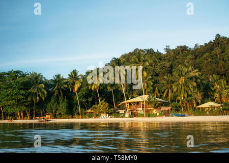 Port Barton, Palawan, Philippines - February 2, 2019: People on tropical beach with trees against wooden hotel at sunset Stock Photo