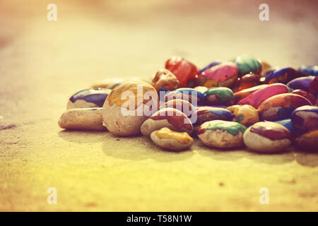 Many small pebbles covered with multicolored paint lie on the surface close-up Stock Photo