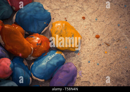 Many small pebbles covered with multicolored paint lie on the surface close-up Stock Photo