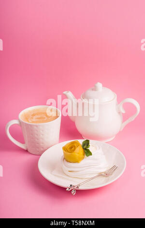 Pavlova dessert from meringue with mango rosette on a white saucer among pink paper tropical leaves on a bright background Stock Photo