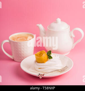 Pavlova dessert from meringue with mango rosette on a white saucer among pink paper tropical leaves on a bright background Stock Photo