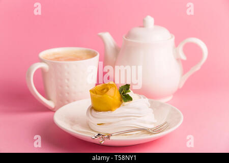 Pavlova dessert from meringue with mango rosette on a white saucer among pink paper tropical leaves on a bright background Stock Photo