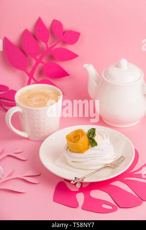 Pavlova dessert from meringue with mango rosette on a white saucer among pink paper tropical leaves on a bright background Stock Photo