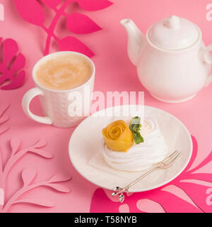 Pavlova dessert from meringue with mango rosette on a white saucer among pink paper tropical leaves on a bright background Stock Photo