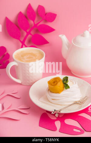 Pavlova dessert from meringue with mango rosette on a white saucer among pink paper tropical leaves on a bright background Stock Photo