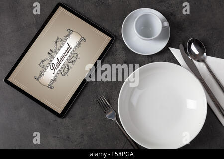 Tablet with stylish restaurant logo and laid table  Stock Photo
