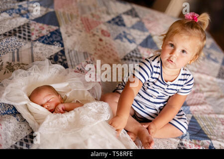 Newborn baby boy in bed. Cute toddler girl playing with her newborn baby brother. Stock Photo