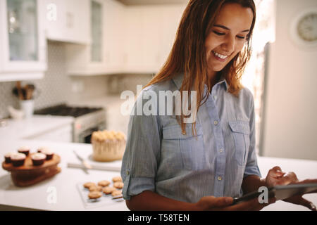 Pastry chef using digital tablet in kitchen. Female confectioner with tablet computer with parties on kitchen counter at the back. Stock Photo