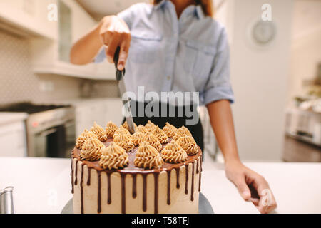 Woman chef cutting a cake while cooking in kitchen at home. Close up of party chef cutting freshly made cake with knife. Stock Photo