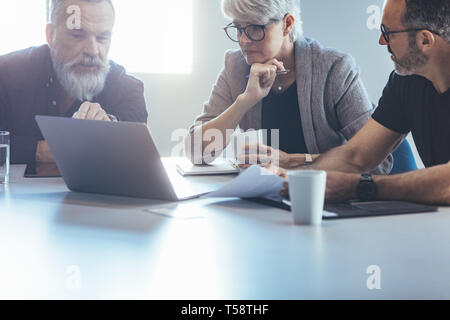 Business team of meeting around a table in office. Group of business man and woman discussing work over a laptop in office. Stock Photo