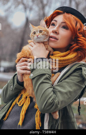 Portrait of a red-haired girl with a red cat outdoor on the street Stock Photo