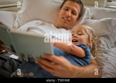 Father lying down reading a book with his daughter. Stock Photo