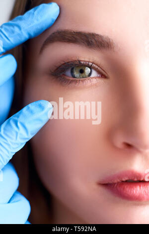 Upper eyelid reduction, double eye lid removal plastic surgery concept. Beautician doctor hands in gloves touching female face skin. Ophthalmologist Stock Photo
