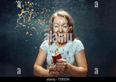 Woman drinking a cola at studio. Young smiling happy caucasian girl opening can with cola and enjoying the spray. Advertising image about favourite drink. Lifestyle and human emotions concept. Stock Photo