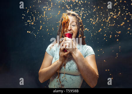 Woman drinking a cola at studio. Young smiling happy caucasian girl opening can with cola and enjoying the spray. Advertising image about favourite drink. Lifestyle and human emotions concept. Stock Photo