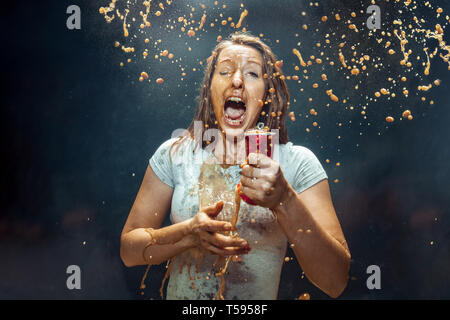 Woman drinking a cola at studio. Young smiling happy caucasian girl opening can with cola and enjoying the spray. Advertising image about favourite drink. Lifestyle and human emotions concept. Stock Photo