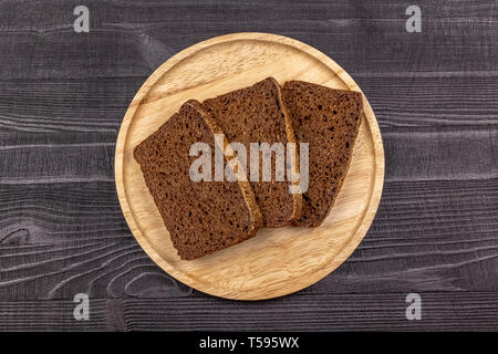 Pieces of rye flour black bread on a wooden serving plate and black rustic background. Top view. Stock Photo