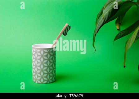 Close up of one bamboo toothbrush in a mug with some leaves on green background with copy space Stock Photo
