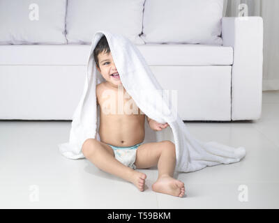 PORTRAIT OF INFANT IN DIAPER WITH HEAD COVERED BY A TOWEL Stock Photo