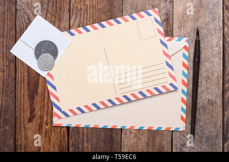 Blank post card with envelope, stamps and coins on wooden table Stock Photo