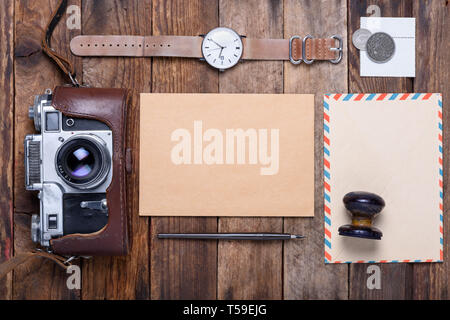 Blank card with envelope and vintage camera, stamps, watch, ink pen on wooden table still life Stock Photo
