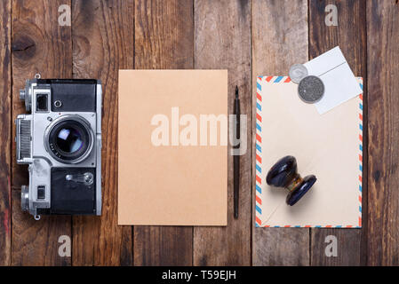 Card with envelope, stamps and retro camera on old wooden table still life Stock Photo