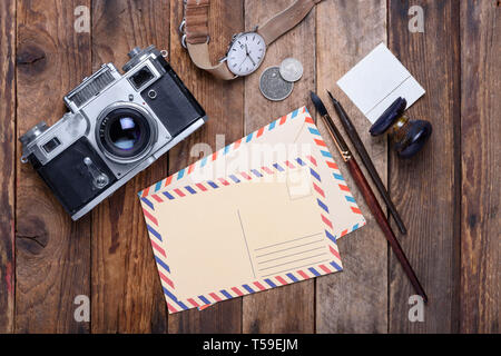 Blank post card with envelope and vintage camera, stamps, watch, ink pen and brush on wooden table still life Stock Photo