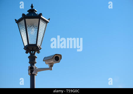 CCTV surveillance camera mounted on vintage street lantern over blue sky background Stock Photo