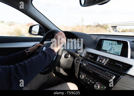 Madrid, Spain - April 1, 2019: Side view of man driving BMW X2 car, with his hands on the steering wheel, using a satelite navigation GPS Stock Photo