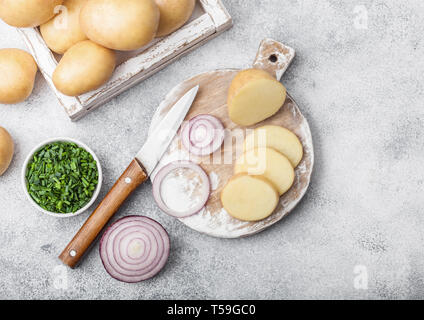 Fresh raw organic potatoes in wooden box and on chopping board with red and green onions on light background Stock Photo