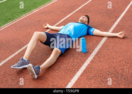 Young sportsman on stadium outside lying on track with bottle of water hands aside smiling relaxed Stock Photo