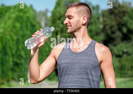 Healthy Lifestyle. Man practicing yoga outdoors standing drinking water happy side view Stock Photo