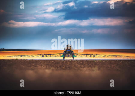 Farming tractor plowing and spraying on field Stock Photo