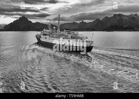 Black And White Image Of The Historic Hurtigruten Ship, MS Lofoten, Steaming Southbound In The Vestfjord, The Rugged Lofoten Islands Behind. Norway. Stock Photo