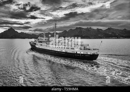A Moody Black And White Image Of The Classic Hurtigruten Ship, MS Lofoten, Steaming In The Vestfjord, The Rugged Lofoten Islands Behind. Norway. Stock Photo