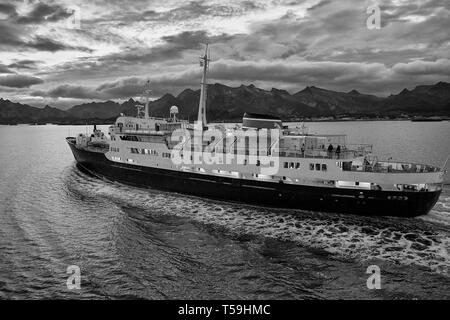 A Moody Black And White Image Of The Vintage Hurtigruten Ferry, MS Lofoten, Steaming Southbound In The Vestfjord, The Lofoten Islands Behind. Norway. Stock Photo