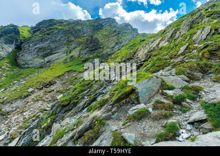 hiking uphill rocky slopes of fagaras mountains. hard path among big and sharp boulders. sunny summer weather with cloudy sky Stock Photo